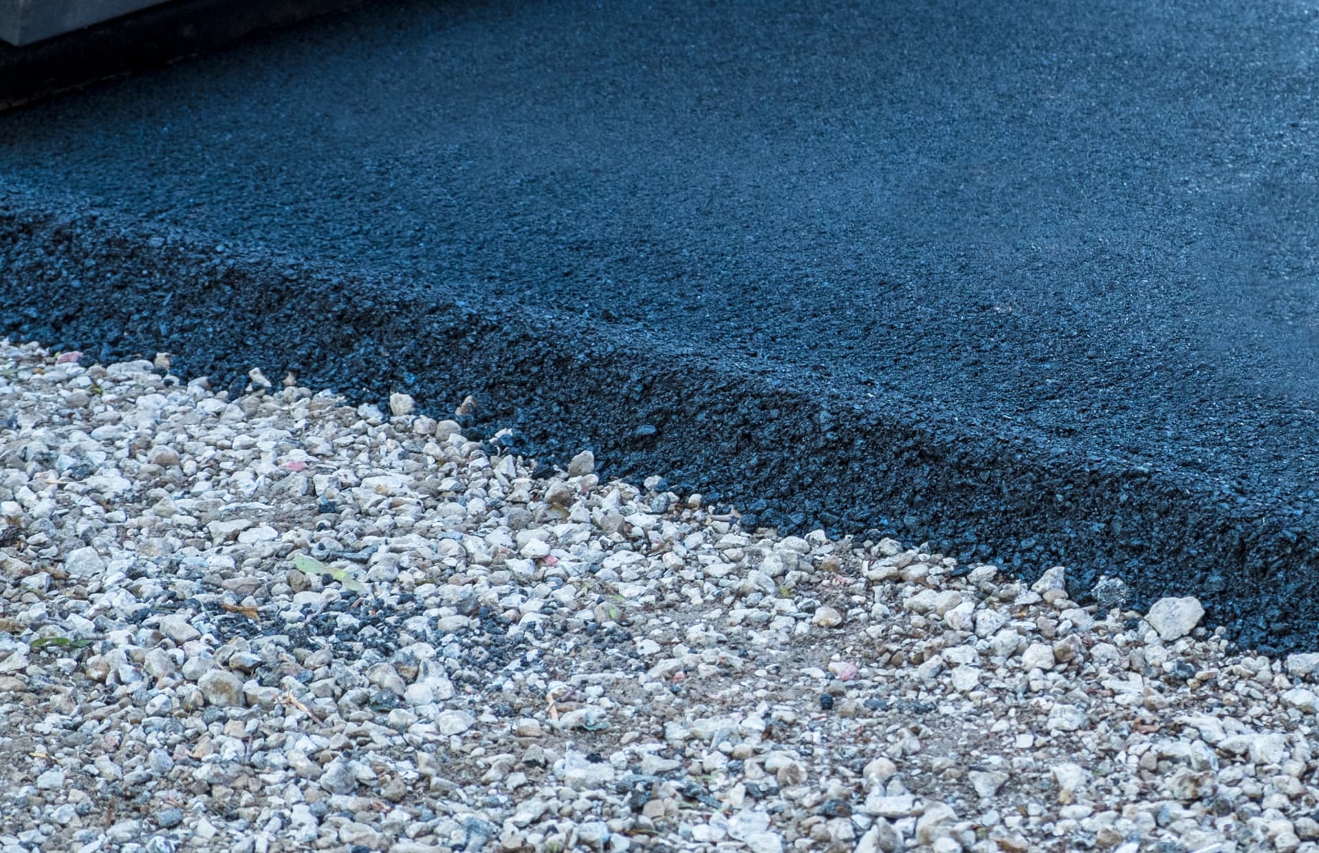 A close view of the edge where fresh black asphalt meets pale gravel.
